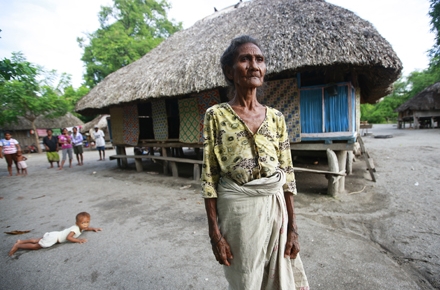 A Timorese women stands in front of traditional housing. Photo by UN Photo on flickr.