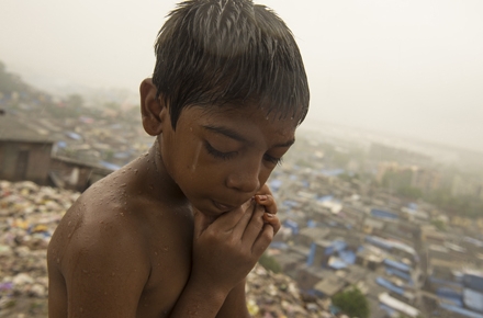 A young boy stands on rubbish in Mumbai's slums. Photo by Brett Davies on flickr.